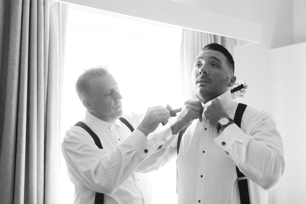 Groom putting on bow tie with the help of his dad