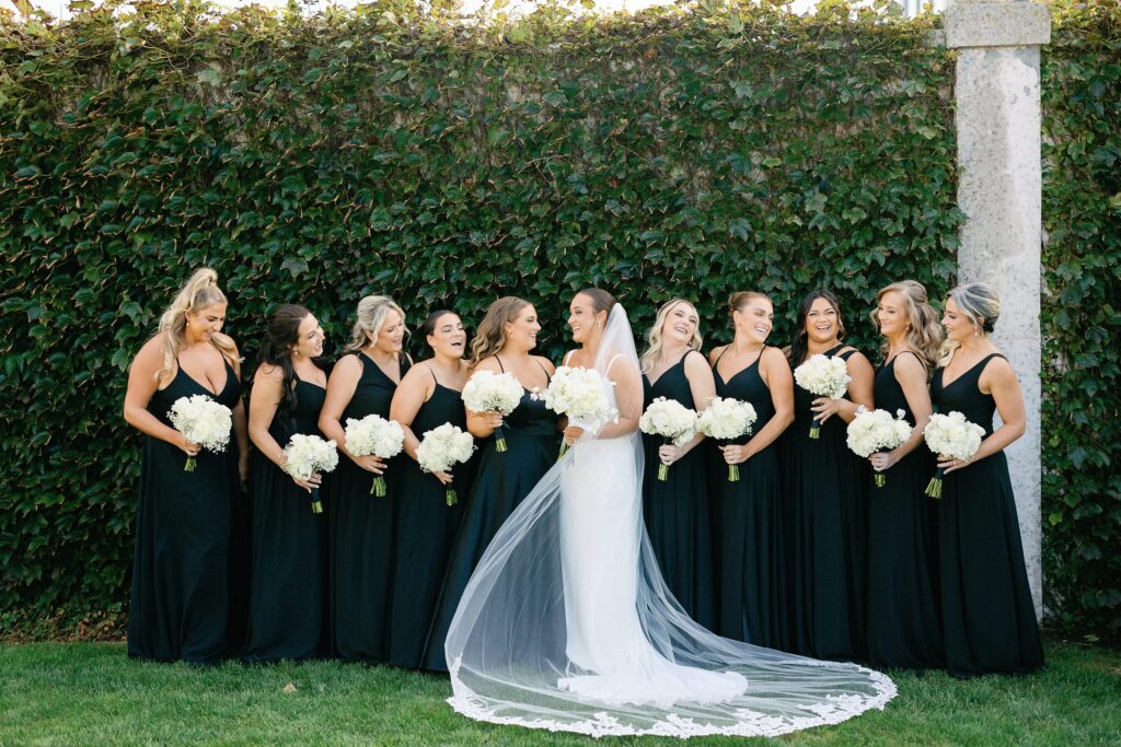 Bride and bridesmaids portrait for Belle Mer wedding in Newport, RI with bridesmaids wearing black dresses