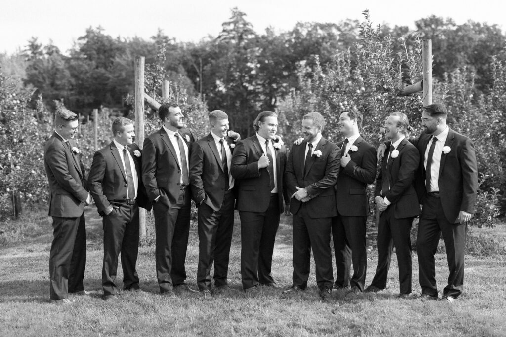 Black and white candid groomsmen portrait in the orchard at The Greenery at McKenzie's Farm Wedding