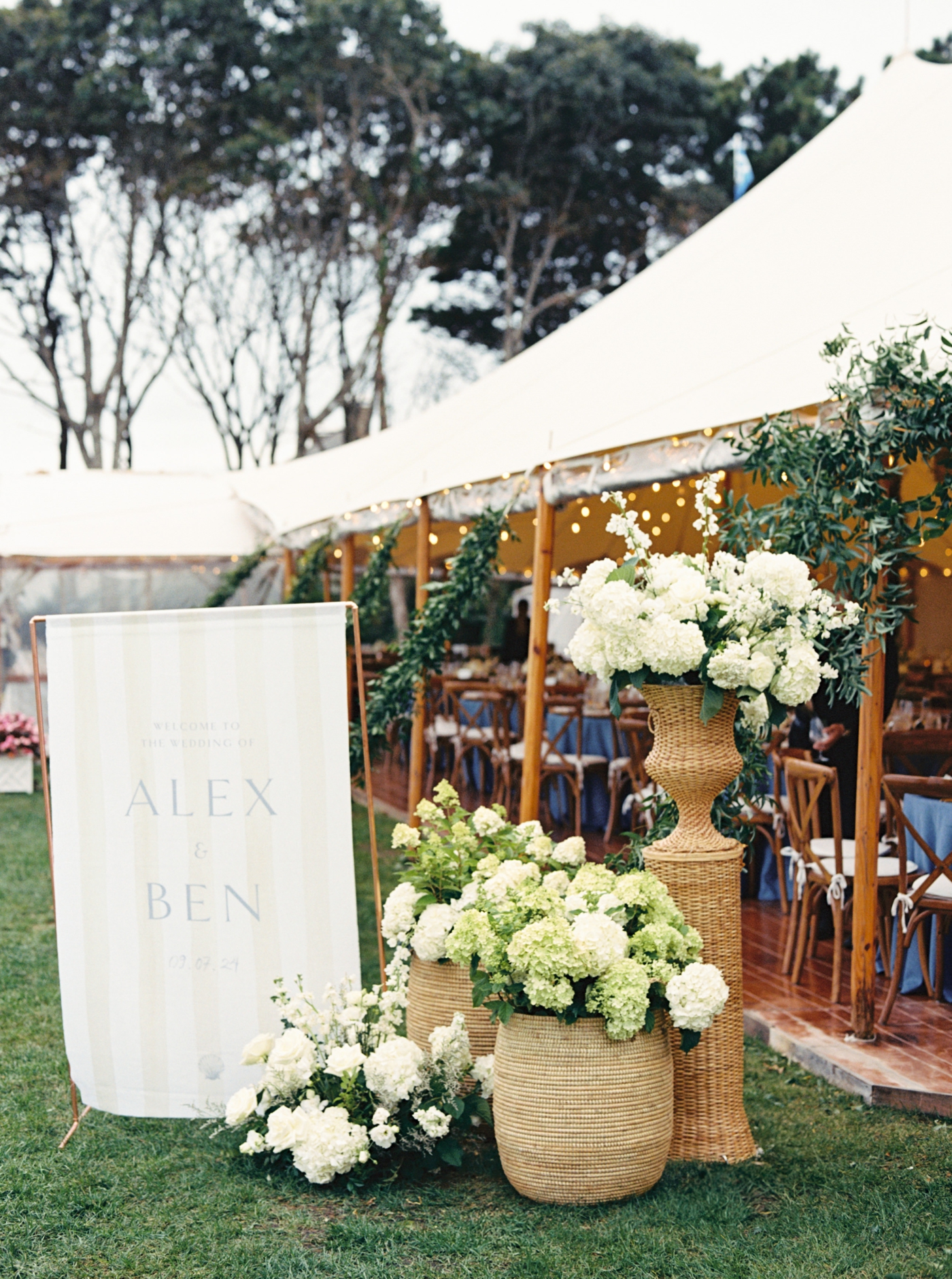 Wedding reception entrance with a custom fabric sign, wicker baskets, and white hydrangeas
